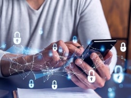 A programmer is browsing the Internet in smart phone to protect a cyber security from hacker attacks and save clients confidential data. Padlock Hologram icons over the typing hands.