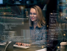 Woman programming on her desk with code blocks on virtual screen.